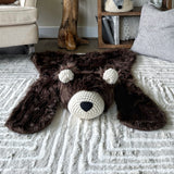 Front view of the brown faux fur bear rug laying flat on a plush cream colored carpet. Highlights the soft fabric texture, cream crochet ears, cream muzzle, and black nose. Woodland nursery decor by ClaraLoo.