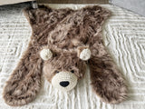 Straight-down overhead view of the cappuccino faux fur bear rug head-on a beige carpet. Perfectly showcases the symmetry of the black safety eyes, cream crochet muzzle, and ears. Cozy woodland nursery decor mat.