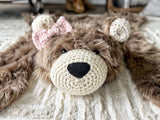 Close-up, straight-on view of the cappuccino faux fur bear rug featuring secure black safety eyes. Detailed head shot on beige carpet showcasing the cream crochet muzzle and ears. Cute animal floor mat for a woodland nursery.