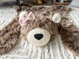 Close-up, straight-on view of the plush cappuccino faux fur bear rug on a beige carpet. Highlights the textured cream crochet muzzle, ears, and black nose details. Ideal for woodland theme nursery floor decor.
