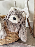 A plush bear lovey made with brown and beige tipped faux fur and cream crochet ears, draped over a tan basket.