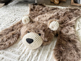 Overhead front angle view of the plush cappuccino faux fur bear rug flat on a beige carpet. Shows the black safety eyes, cream crochet muzzle, and cream ears. A cozy handmade animal floor mat for a woodland theme nursery.
