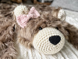 Side angle view of the cappuccino faux fur bear rug head with black safety eyes. A pink crochet bow is attached below the right ear, appearing on the left side of the photo. Cozy accent rug for a woodland kids bedroom.