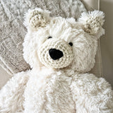 A close-up view of a white plush polar bear stuffed animal focusing on its head and upper body to show the detail of its black safety eyes and crochet accents.