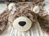 Close-up head view of the cappuccino faux fur bear rug with black safety eyes. Features light purple and green crochet flowers attached below the right ear, on the left side of the photo. Detailed texture shot for a woodland nursery.