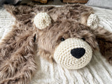 Close-up front angle view focusing on the right side of the cappuccino faux fur bear rug head. Shows the textured plush fabric, black safety eyes, and cream crochet details on beige carpet. Cozy woodland nursery decor.